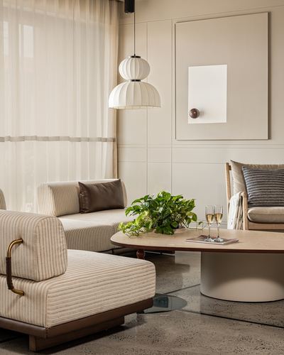 Living room with striped sofas, cane armchair, oval coffee table and layered pendant beside sheer curtains