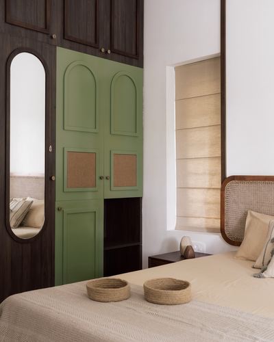 Bedroom corner with green arched wardrobe doors, cane headboard bed, and woven jute baskets