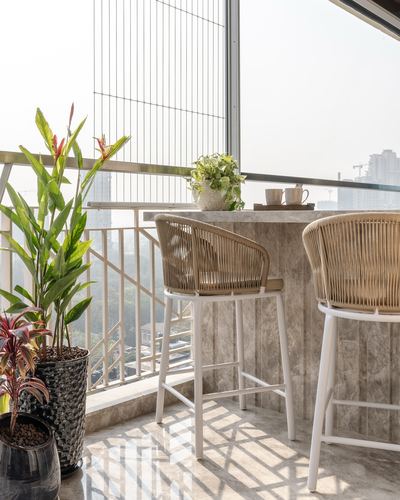 Balcony with stone-clad bar counter, two woven stools, potted plants and city skyline view