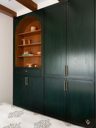Arched wooden shelf niche set into a dark green wardrobe wall with brass handles