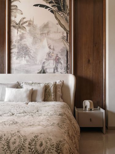 Bedroom with upholstered headboard beneath a painted mural panel, fluted nightstand, and floral bedspread