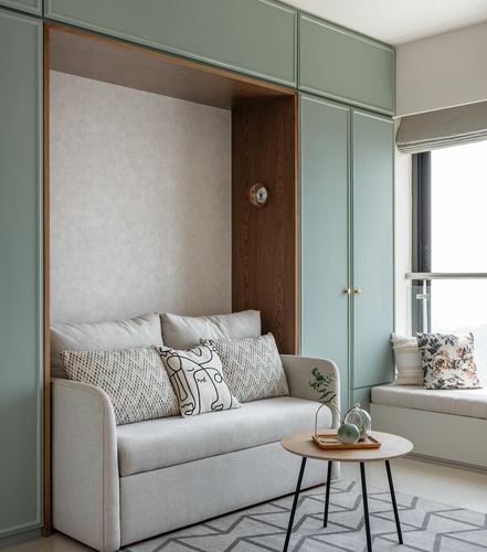 Sage green built-in cabinetry with recessed wood niche housing a beige sofa, window seat beside it