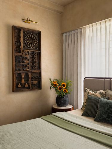 Bedroom corner with carved wooden panel, sunflowers, and olive green bedding against warm plaster wall