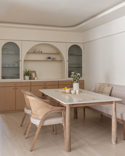Cream dining room with arched wood shelving, glass cabinets, cane chairs and a stone-top table