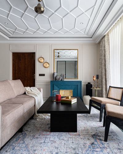 Living room with patterned white ceiling, teal fireplace surround, black coffee table and cane armchairs on a blue rug