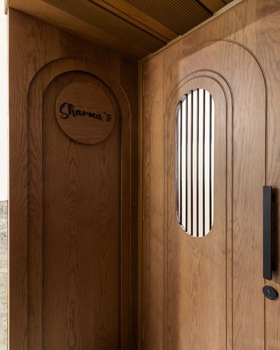 Arched wooden entry door with fluted glass panel and circular nameplate reading Sharma's