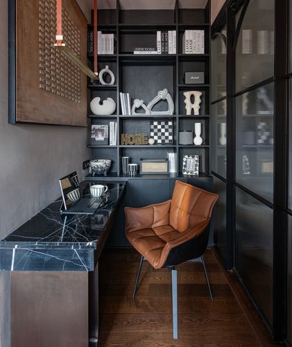 Compact home office with black marble desk, dark bookshelf, and tan leather chair