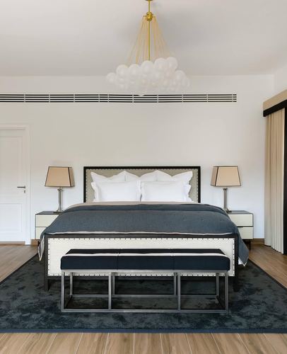 Symmetrical bedroom with navy bedding, striped bench, and a bubble chandelier overhead