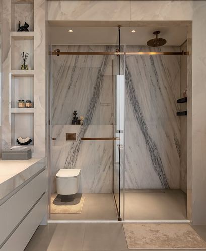 Marble-clad bathroom with glass-enclosed shower, brass fixtures, and floating vanity
