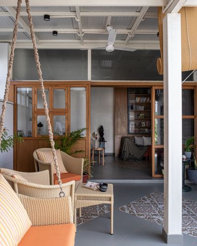 Covered veranda with woven swing chairs, potted plants and view into a study with bookshelf