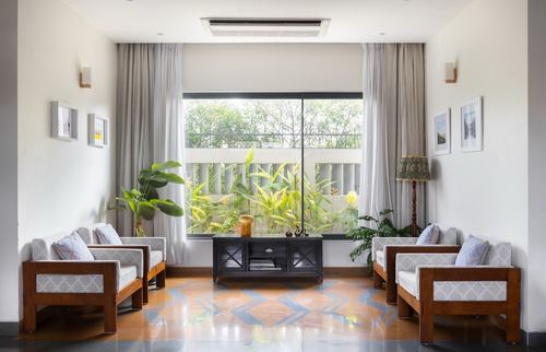Symmetrical living room with wooden armchairs facing a large window with garden view and patterned floor inlay
