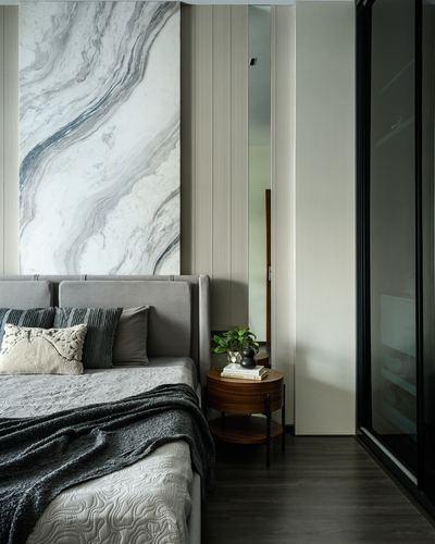 Bedroom with grey upholstered bed, marble accent wall, and round wood nightstand with mirror