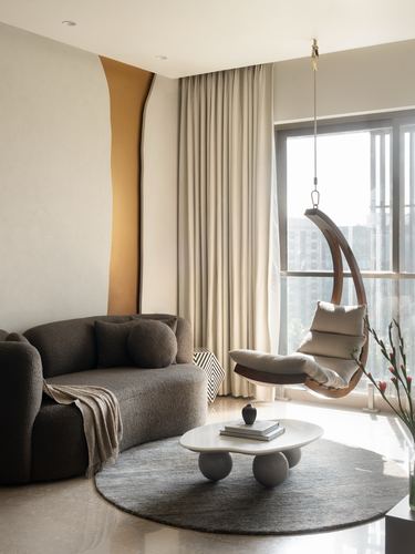 Living room with curved boucle sofa, hanging wooden egg chair, and sculptural marble coffee table by a window