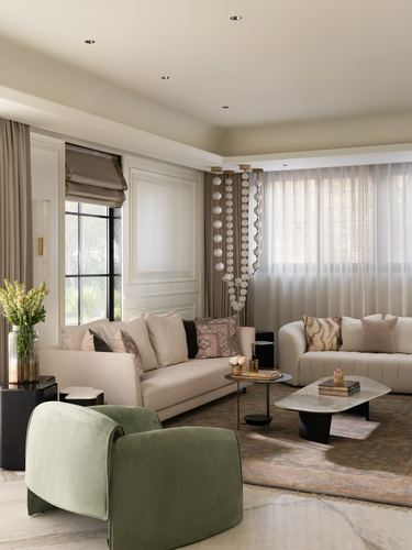 Neutral living room with sage armchair, beige sofas, and cascading pendant lights by curtained windows