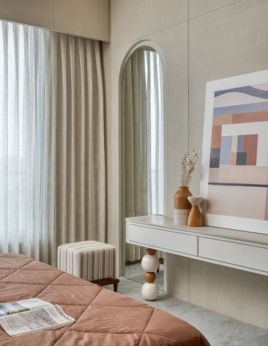 Bedroom corner with arched mirror, console table, abstract art, and pink quilted bed against sheer curtains