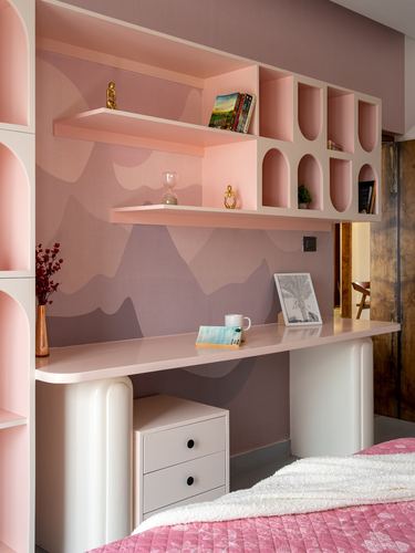 Pink built-in desk and shelving unit with arched niches against a mauve mountain-print wall