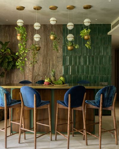 Dining island with blue velvet stools, hanging plants, brass pendants, and green ribbed tile wall