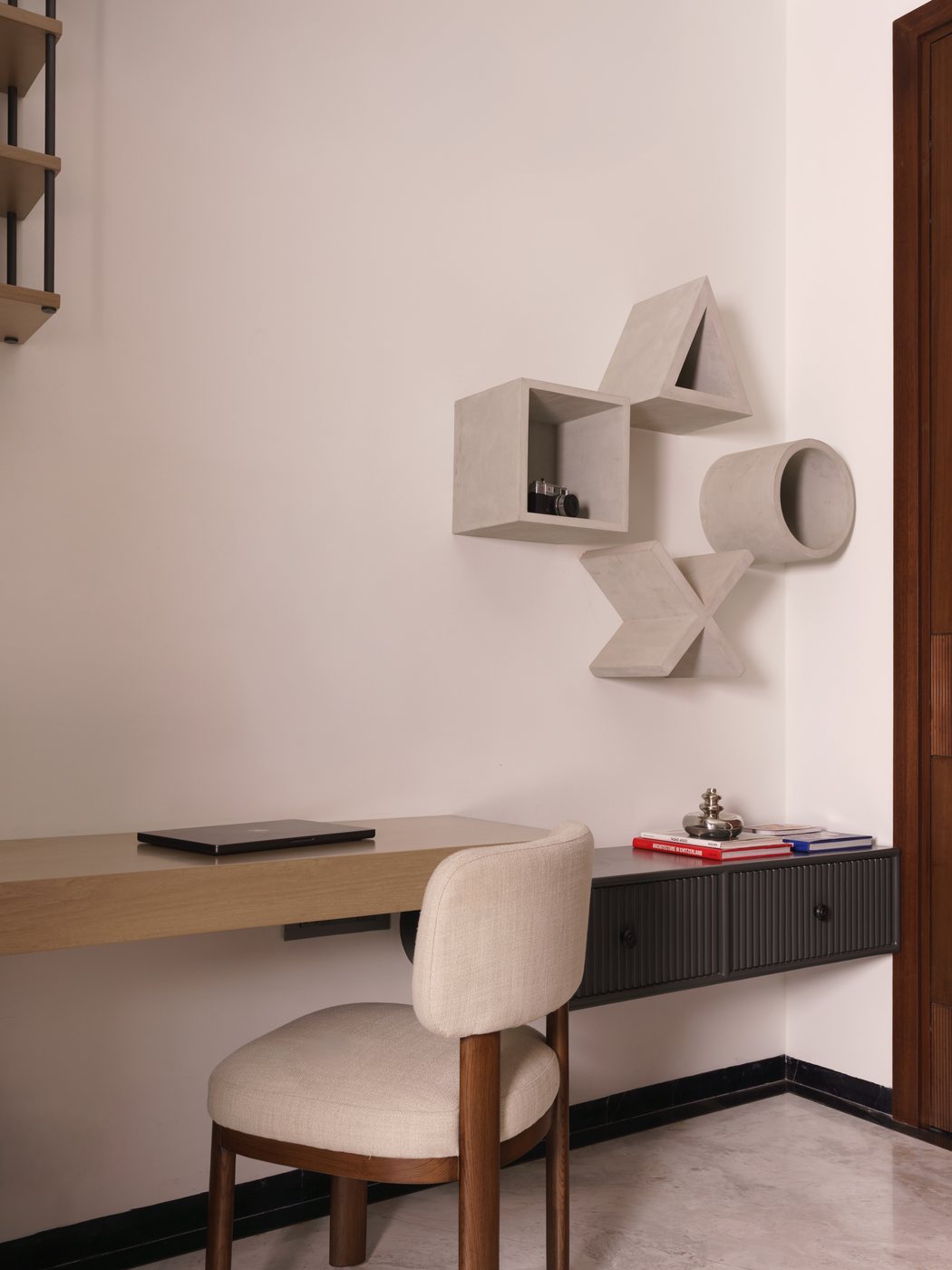 Minimalist study nook with floating wood desk, upholstered chair and sculptural geometric wall shelves