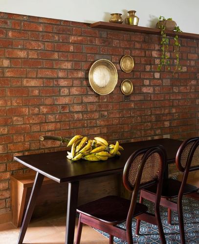 Dining table before exposed brick wall with brass plates, urlis, and cane bentwood chairs
