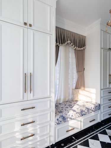 White paneled wardrobe wall with recessed window seat, floral cushion, and marble floor