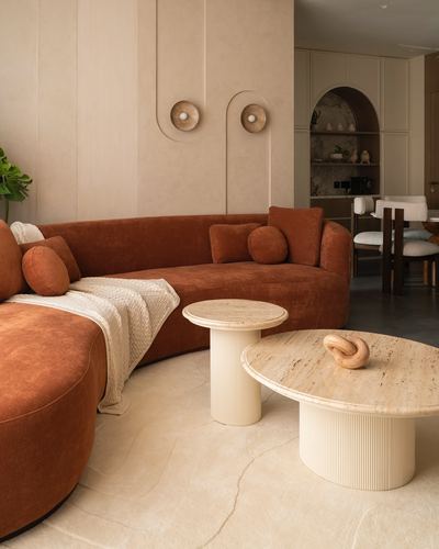Curved terracotta velvet sofa with round travertine coffee tables in a warm-toned living room