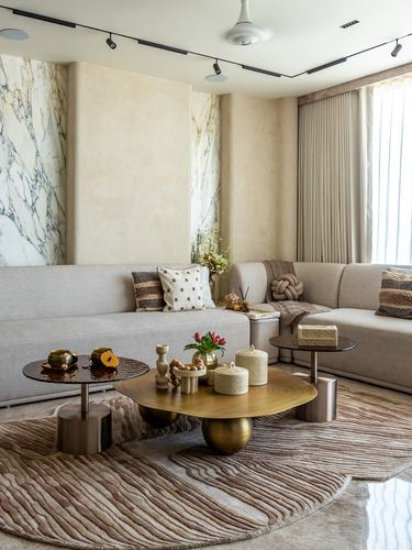 Beige sectional sofa with layered round brass coffee tables on a striped rug beneath marble-clad wall panels