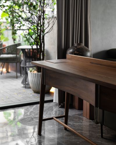 Wooden desk beside marble floor and glass door opening to a planted terrace
