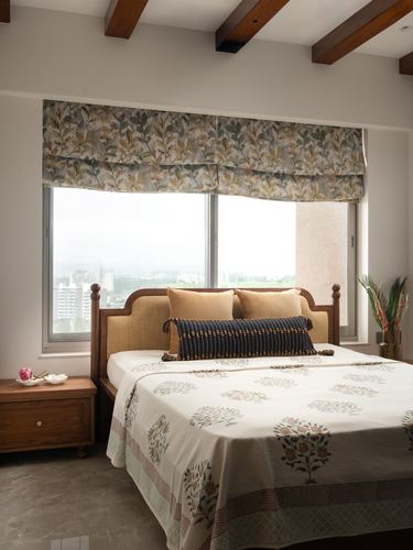 Bedroom with cane headboard, floral roman blinds, exposed wood beams, city view through windows