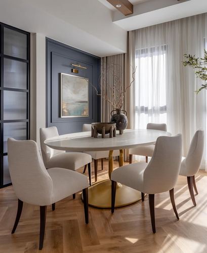 Oval dining table with beige upholstered chairs against navy paneled wall and sheer curtains