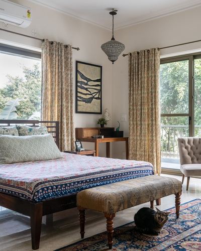 Bedroom with wooden bed, patterned curtains, pendant lantern, and a cat resting on a carved bench
