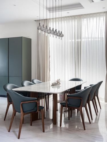 Dining room with marble table, blue-grey leather chairs, and cascading pendant lights before sheer curtains