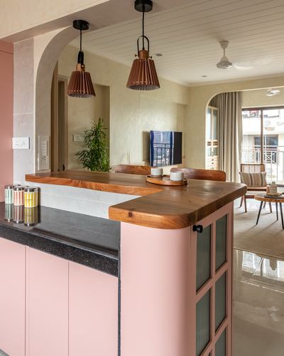 Pink kitchen counter with curved wood top framed by an arch, living room beyond