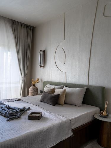 Bedroom with green upholstered headboard against a textured plaster wall with linear inlay design