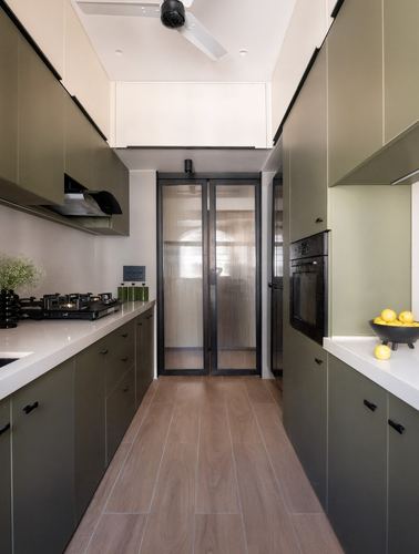 Parallel galley kitchen with olive cabinetry, white stone counters, wood-look tile floor, ending at a reeded glass door.