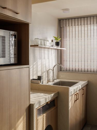 Sunlit minimal kitchen corner with wood cabinetry, stone sink counter, and striped window shade
