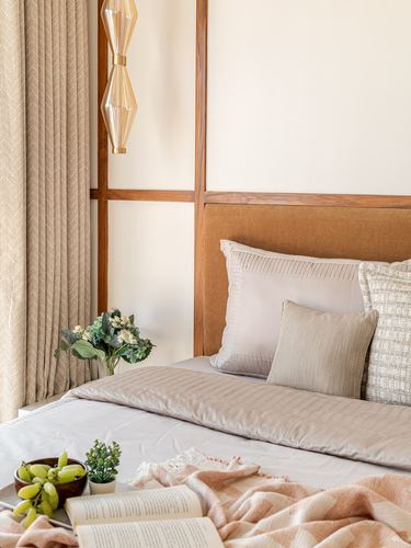 Bedroom corner with tan upholstered headboard, wood wall panelling, and layered cushions in warm light