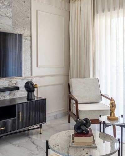 Living room corner with fluted black console, textured stone wall, cream armchair and sculptural objects
