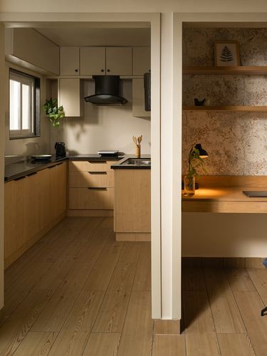 Wooden kitchen with black countertop beside a wallpapered study nook with floating desk