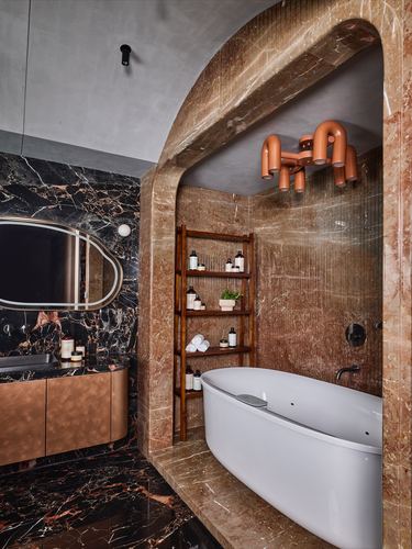 Arched red marble niche housing a freestanding tub beside black marble vanity wall