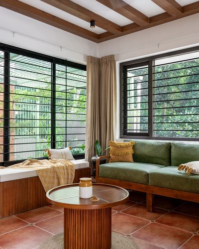 Living room corner with green velvet sofa, wooden window seat, terracotta floor and garden views