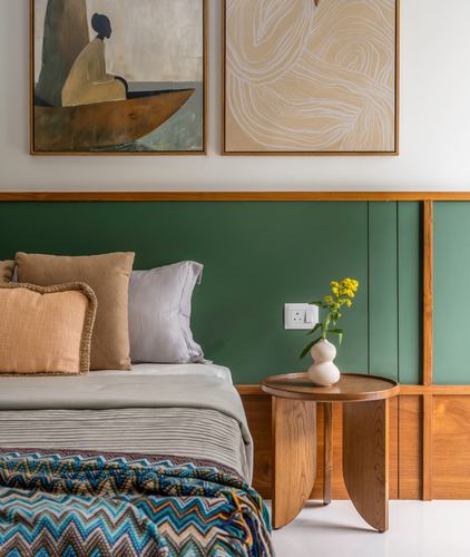 Bedroom with green paneled wall, teak side table, and layered cushions on bed