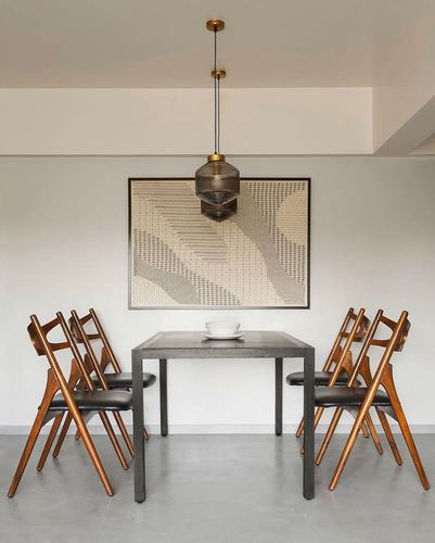 Minimalist dining area with wooden chairs, dark table, brass pendant light and textile artwork