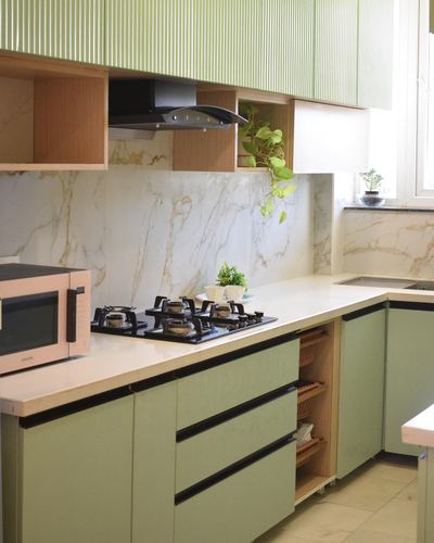 Sage green modular kitchen with marble-look backsplash, black hob, and wood-toned open shelving unit