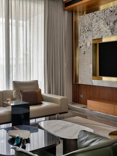 Living room with beige sofa, sheer curtains, and a brass-framed stone tv wall.