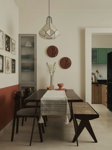 Dining room with dark wood table, cane bench, terracotta wall accents and geometric pendant light