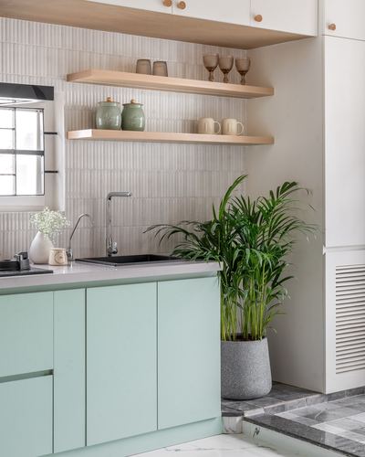 Kitchen counter with mint cabinets, ribbed tile backsplash, wood shelves, and a potted palm