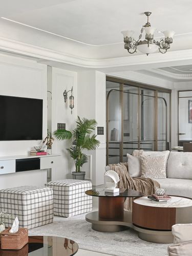 Living room with cream sofa, checkered ottomans, round wood coffee tables and brass chandelier