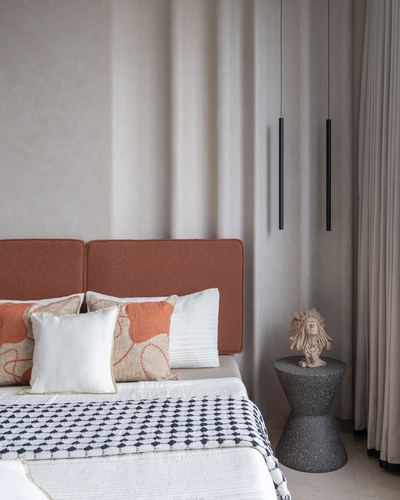 Bedroom corner with terracotta upholstered headboard, patterned pillows, and slim black pendant lights beside a terrazzo side table