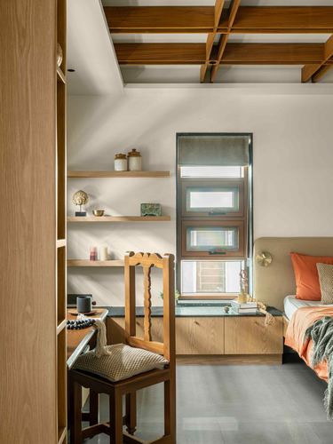 Bedroom corner with carved wooden chair, floating shelves, window seat, and timber ceiling beams