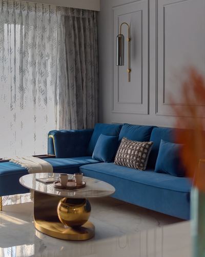 Blue velvet sectional sofa with marble and brass coffee table in a bright paneled living room